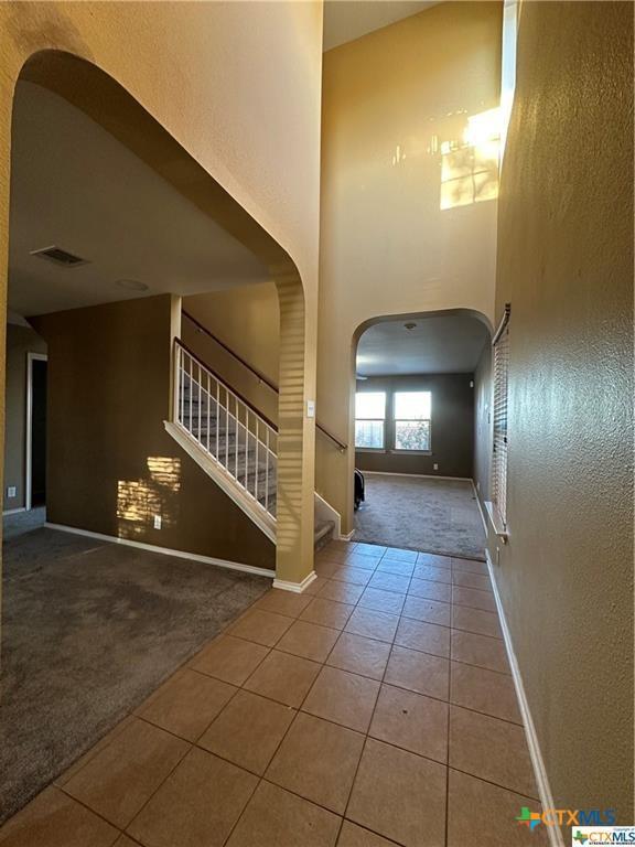 tiled foyer featuring stairs, visible vents, carpet floors, arched walkways, and baseboards