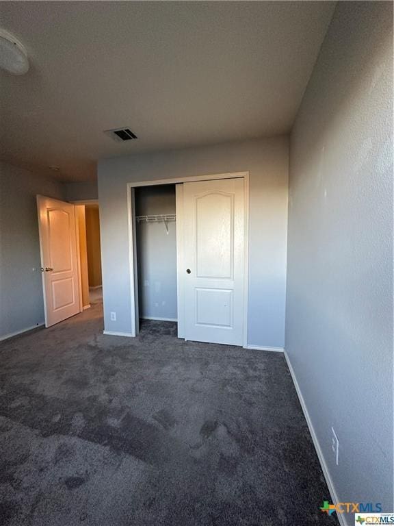 unfurnished bedroom with a closet, visible vents, baseboards, and dark colored carpet