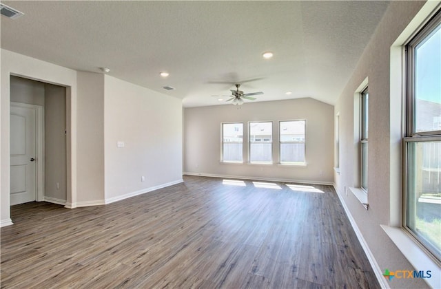 spare room with a textured ceiling, hardwood / wood-style floors, a healthy amount of sunlight, and vaulted ceiling