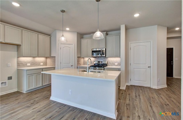 kitchen featuring a kitchen island with sink, sink, decorative backsplash, light wood-type flooring, and stainless steel appliances