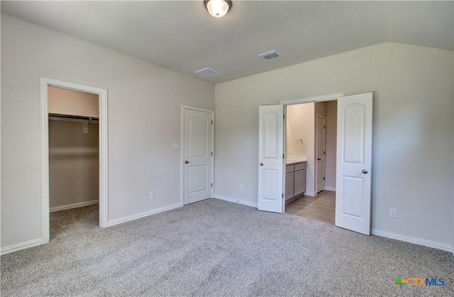 unfurnished bedroom featuring ensuite bathroom, light colored carpet, vaulted ceiling, a spacious closet, and a closet