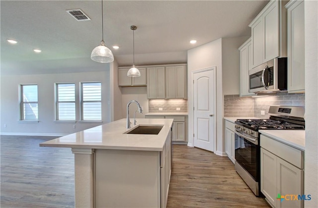 kitchen featuring a center island with sink, white cabinets, sink, light wood-type flooring, and stainless steel appliances