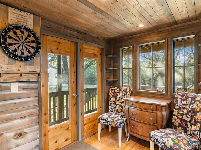 sitting room featuring wooden walls, wooden ceiling, a healthy amount of sunlight, and light hardwood / wood-style flooring