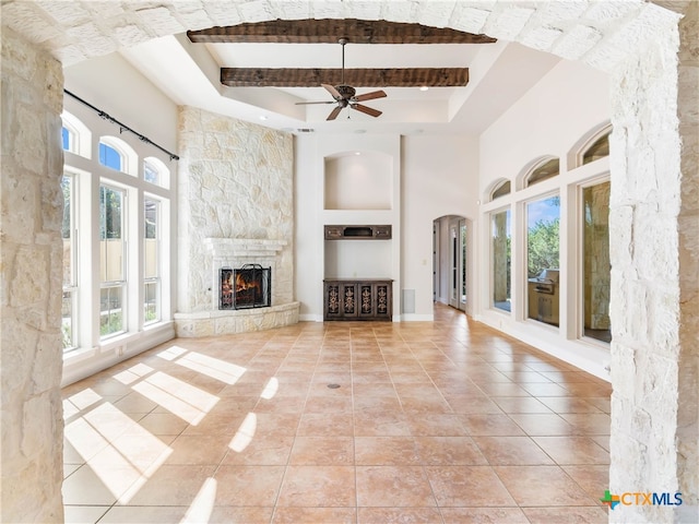 unfurnished living room with light tile patterned flooring, a fireplace, a towering ceiling, beamed ceiling, and ceiling fan