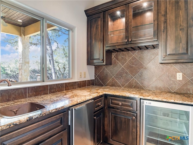 kitchen with beverage cooler, sink, dark brown cabinetry, and light stone countertops