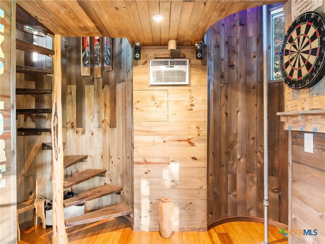 interior space with wooden ceiling, wood-type flooring, wooden walls, and an AC wall unit