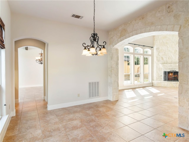 unfurnished dining area with a stone fireplace, a chandelier, and light tile patterned floors