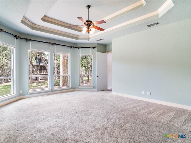 carpeted empty room with crown molding, a wealth of natural light, ceiling fan, and a raised ceiling