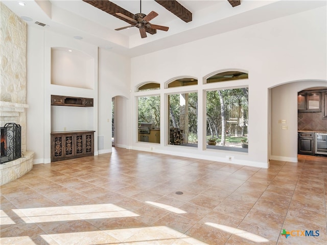 unfurnished living room with a stone fireplace, beamed ceiling, a high ceiling, and wine cooler