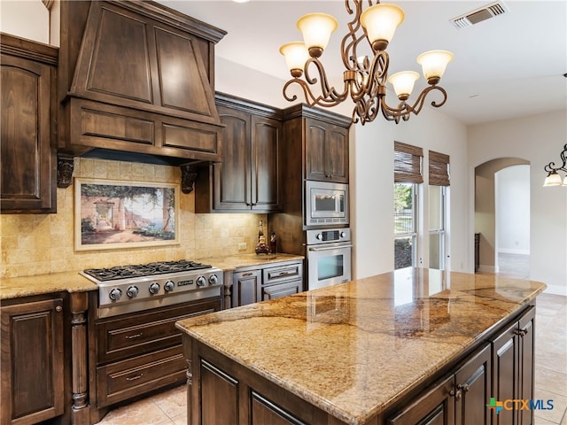 kitchen with hanging light fixtures, light stone counters, stainless steel appliances, and dark brown cabinetry