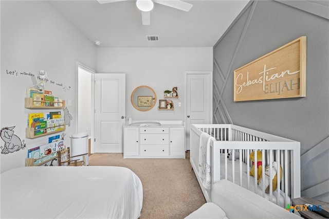 bedroom with a nursery area, light carpet, and ceiling fan