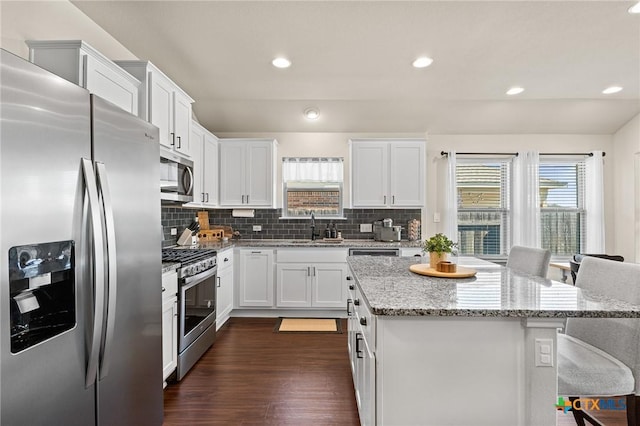 kitchen with stainless steel appliances, a center island, a kitchen bar, and light stone countertops