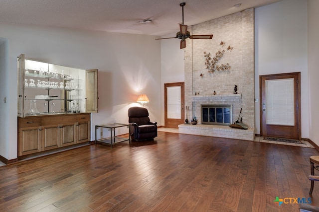 living area featuring high vaulted ceiling, dark hardwood / wood-style flooring, ceiling fan, and a fireplace