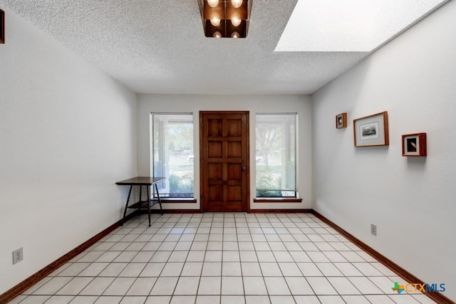 entrance foyer with an inviting chandelier, a textured ceiling, a skylight, and light tile patterned floors