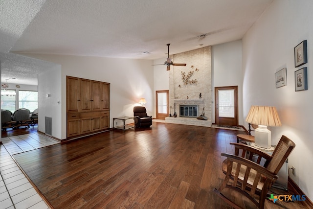 living room featuring a brick fireplace, a textured ceiling, hardwood / wood-style flooring, high vaulted ceiling, and ceiling fan