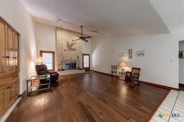 sitting room featuring ceiling fan, a textured ceiling, high vaulted ceiling, hardwood / wood-style floors, and a fireplace