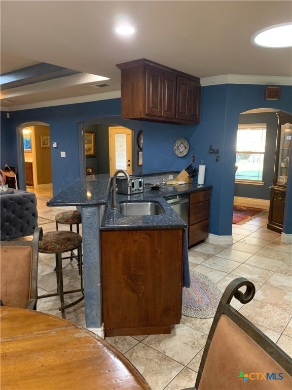 kitchen featuring arched walkways, ornamental molding, a breakfast bar area, and a sink