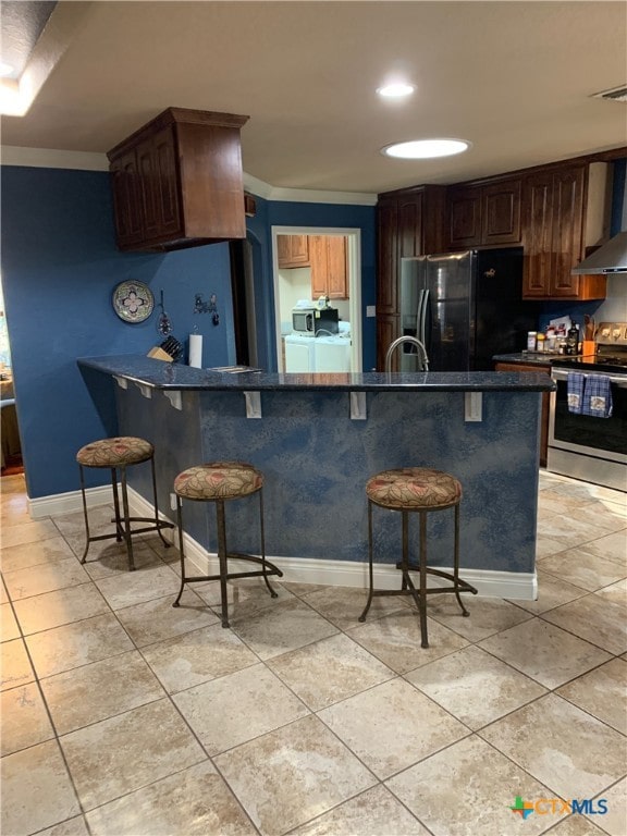 kitchen with dark countertops, a kitchen breakfast bar, freestanding refrigerator, stainless steel range with electric cooktop, and separate washer and dryer