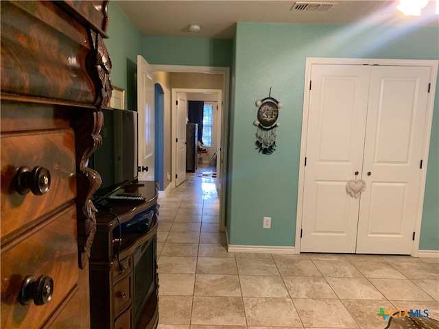 hallway with visible vents, baseboards, and light tile patterned floors