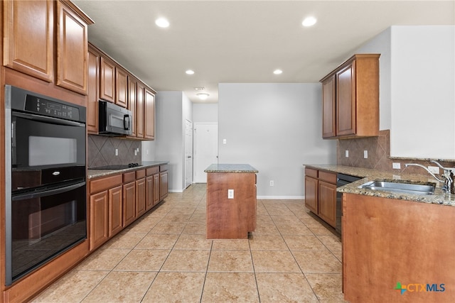 kitchen featuring decorative backsplash, light stone counters, sink, black appliances, and a center island