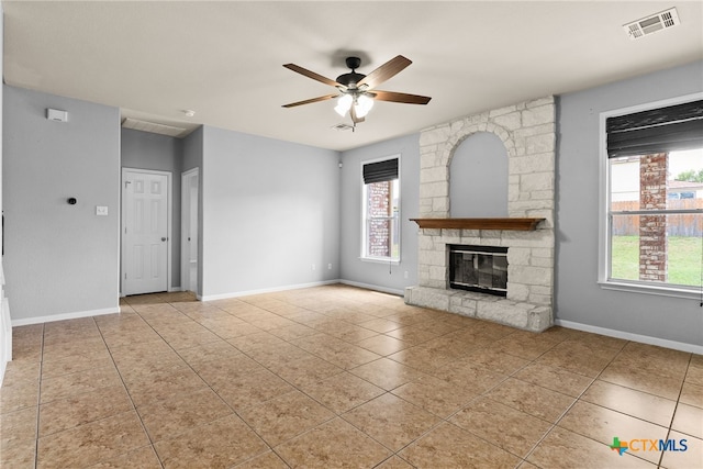 unfurnished living room with a stone fireplace, ceiling fan, and light tile patterned floors