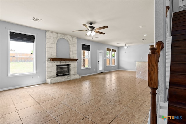 unfurnished living room with a stone fireplace, ceiling fan, and light tile patterned floors