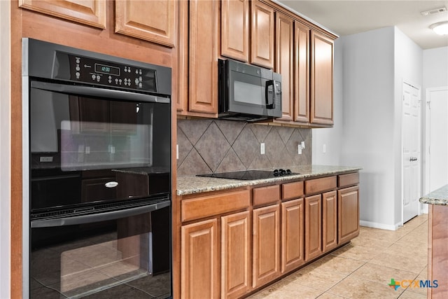 kitchen featuring black appliances, light stone counters, light tile patterned floors, and tasteful backsplash