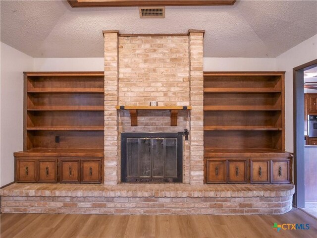 unfurnished living room featuring visible vents, a brick fireplace, a textured ceiling, and wood finished floors