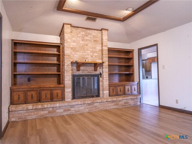 unfurnished living room with baseboards, a textured ceiling, a brick fireplace, and wood finished floors
