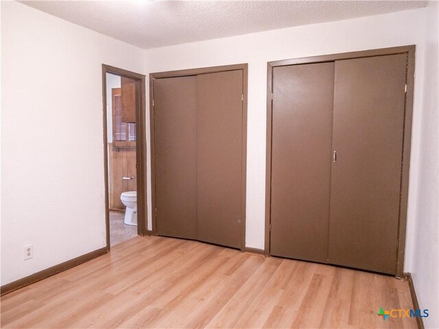 unfurnished bedroom featuring wood finished floors, baseboards, ensuite bath, and two closets