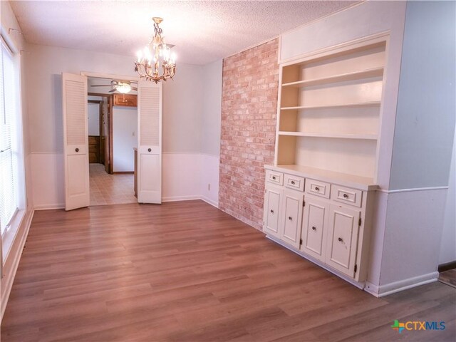 unfurnished dining area featuring light wood-style floors, built in features, a textured ceiling, and a chandelier