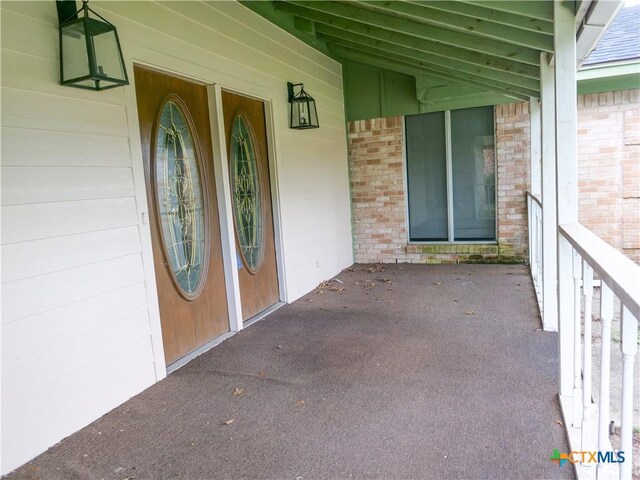 view of exterior entry featuring covered porch and brick siding