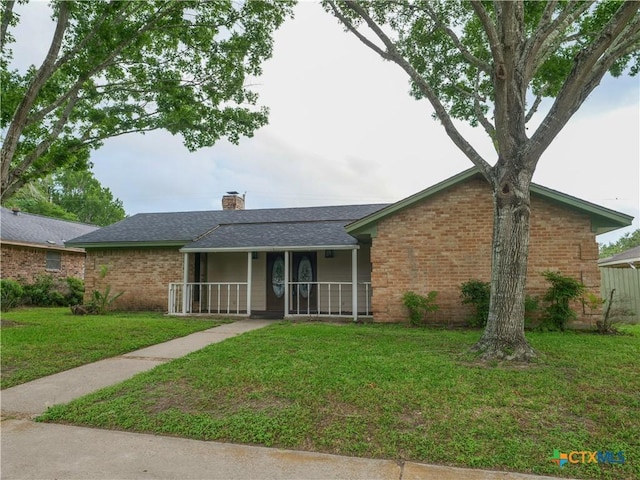 ranch-style house with a shingled roof, a front lawn, brick siding, a chimney, and covered porch