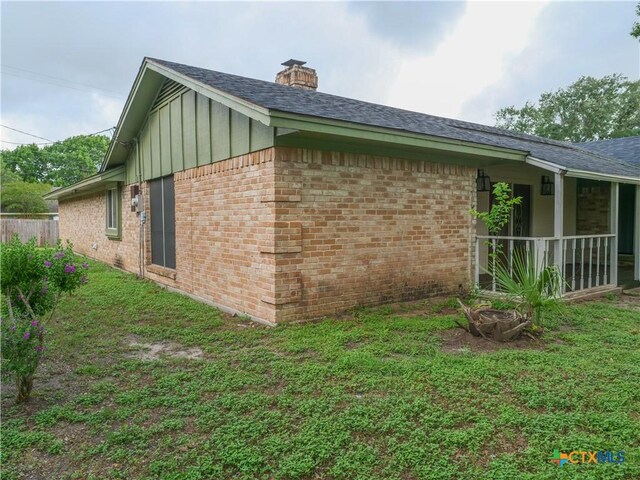 view of home's exterior featuring board and batten siding, a chimney, a lawn, brick siding, and a shingled roof