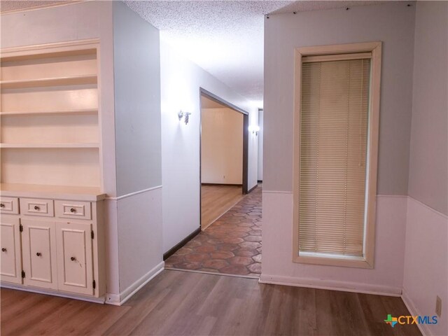 corridor with a textured ceiling, baseboards, and wood finished floors