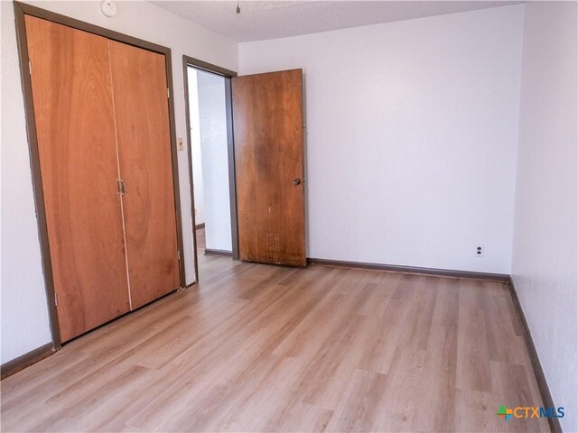 unfurnished bedroom with light wood-type flooring, baseboards, and a closet