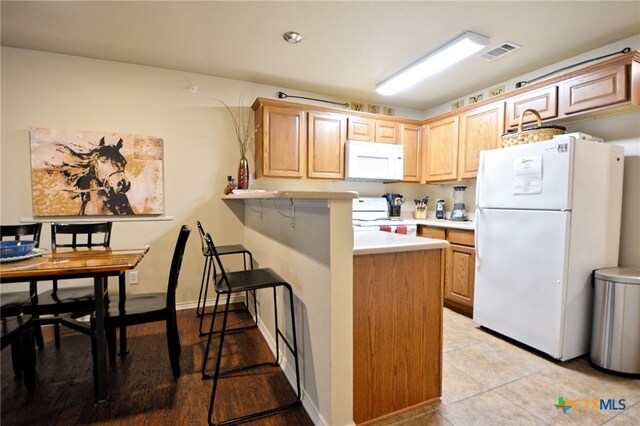 kitchen featuring light tile patterned flooring, kitchen peninsula, light brown cabinetry, a breakfast bar area, and white appliances