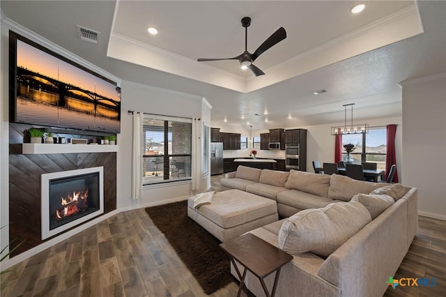 living room with dark wood-type flooring, a glass covered fireplace, a raised ceiling, and visible vents