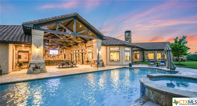 pool at dusk with a patio and an in ground hot tub