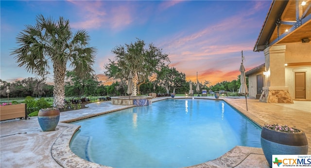 pool at dusk with a patio and an in ground hot tub