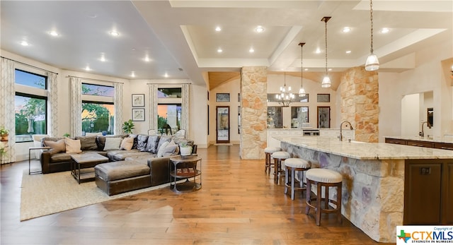 interior space with light hardwood / wood-style floors, a large island with sink, light stone counters, decorative light fixtures, and a tray ceiling