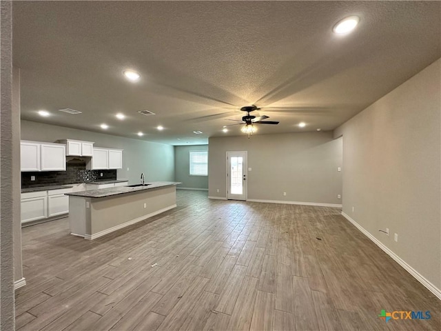 kitchen with white cabinets, ceiling fan, light hardwood / wood-style floors, and an island with sink