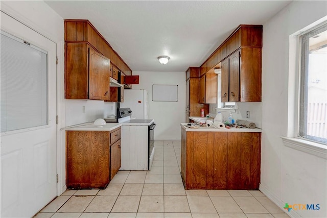 kitchen featuring light tile patterned floors, light countertops, white appliances, and brown cabinetry