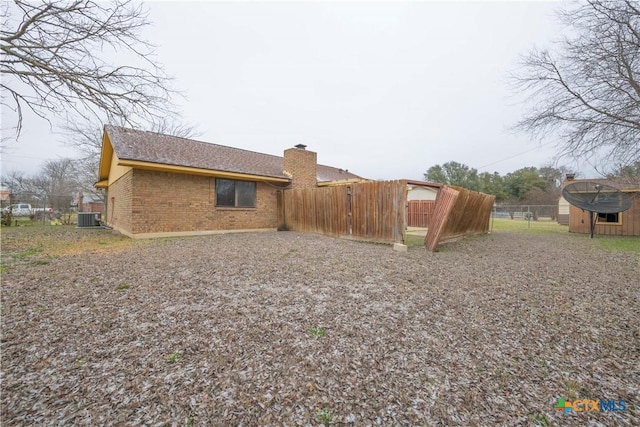 exterior space with an outbuilding, brick siding, a chimney, central air condition unit, and fence