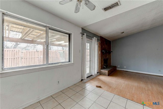 unfurnished living room with visible vents, a brick fireplace, light tile patterned flooring, vaulted ceiling, and ceiling fan