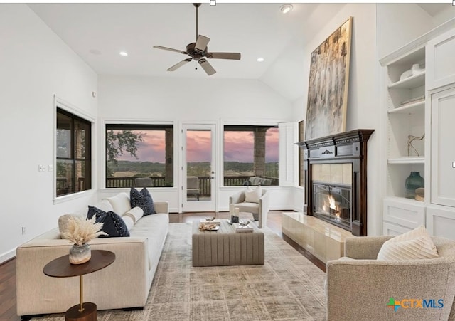 living room featuring a tile fireplace, vaulted ceiling, built in features, hardwood / wood-style flooring, and ceiling fan