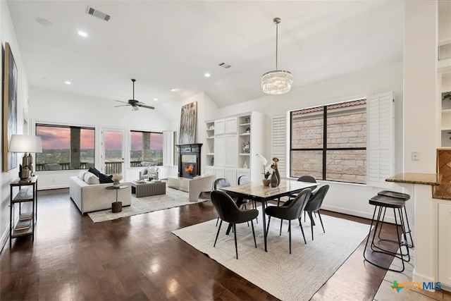 dining space featuring lofted ceiling, ceiling fan with notable chandelier, and dark hardwood / wood-style flooring