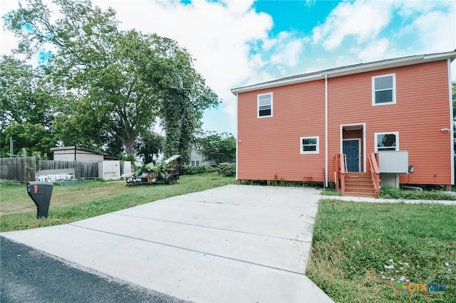 rear view of property featuring fence, a yard, and concrete driveway