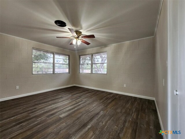 unfurnished room featuring dark wood-style floors, concrete block wall, crown molding, a ceiling fan, and baseboards