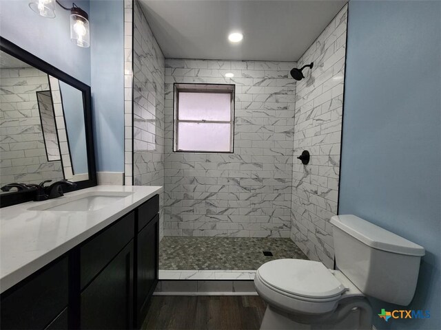 bathroom with a tile shower, vanity, toilet, and wood finished floors